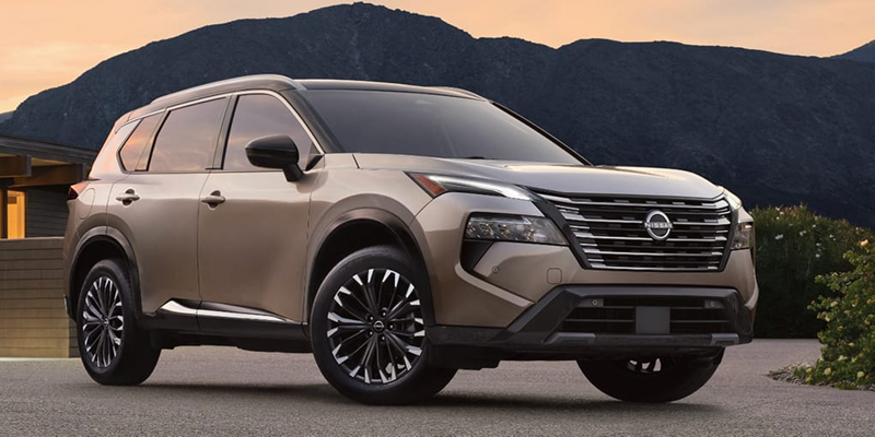 A tan Nissan SUV parked in front of mountains.