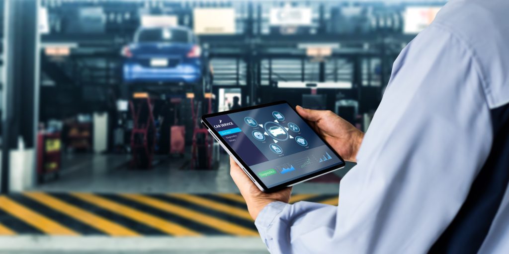Technician using a tablet for car diagnostics in a garage.