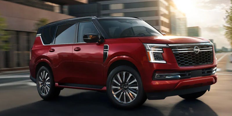 A red Nissan Armada SUV driving on a city street with modern buildings in the background.