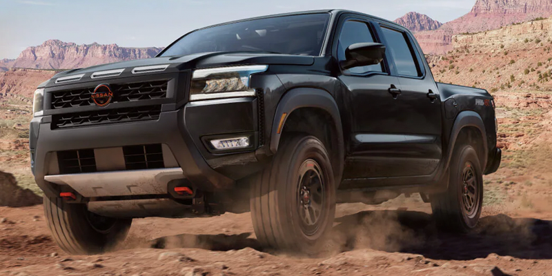 A black Nissan Frontier pickup truck driving through a rocky desert landscape.