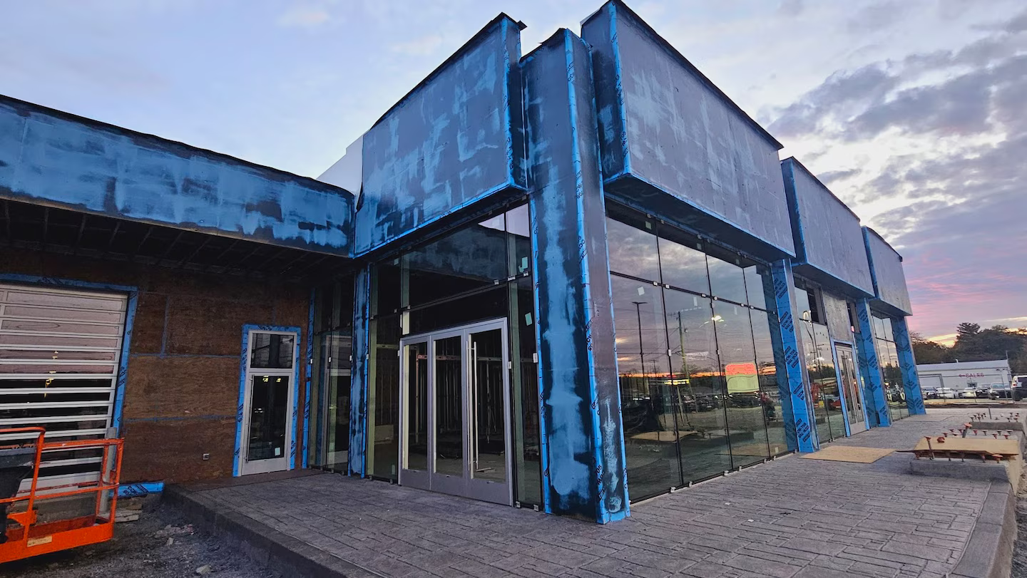 Close-up of dealership building under renovation with blue exterior wrap and glass walls.