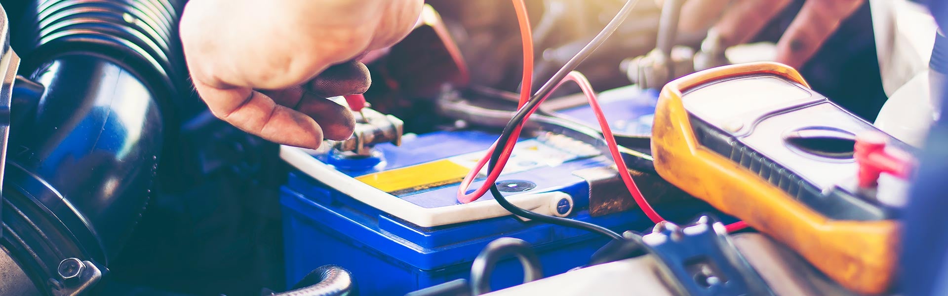 A technician testing a car battery with a digital multimeter in the engine compartment.