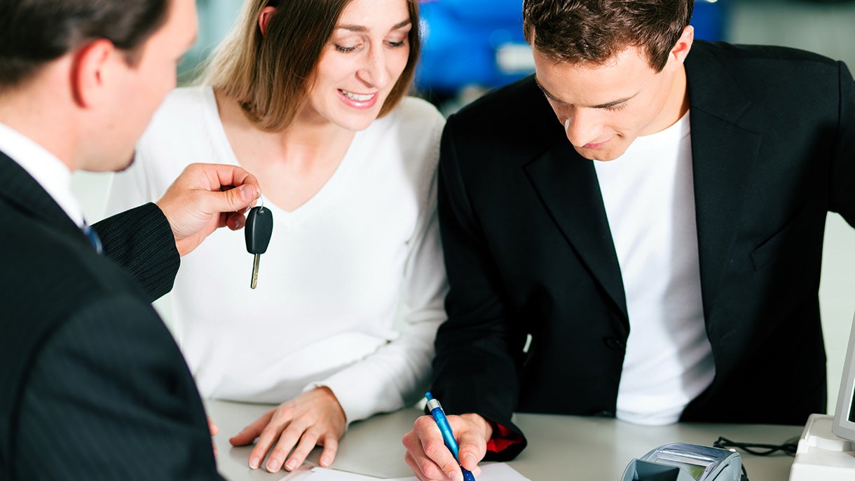 Couple signing papers as salesman hands over a key
