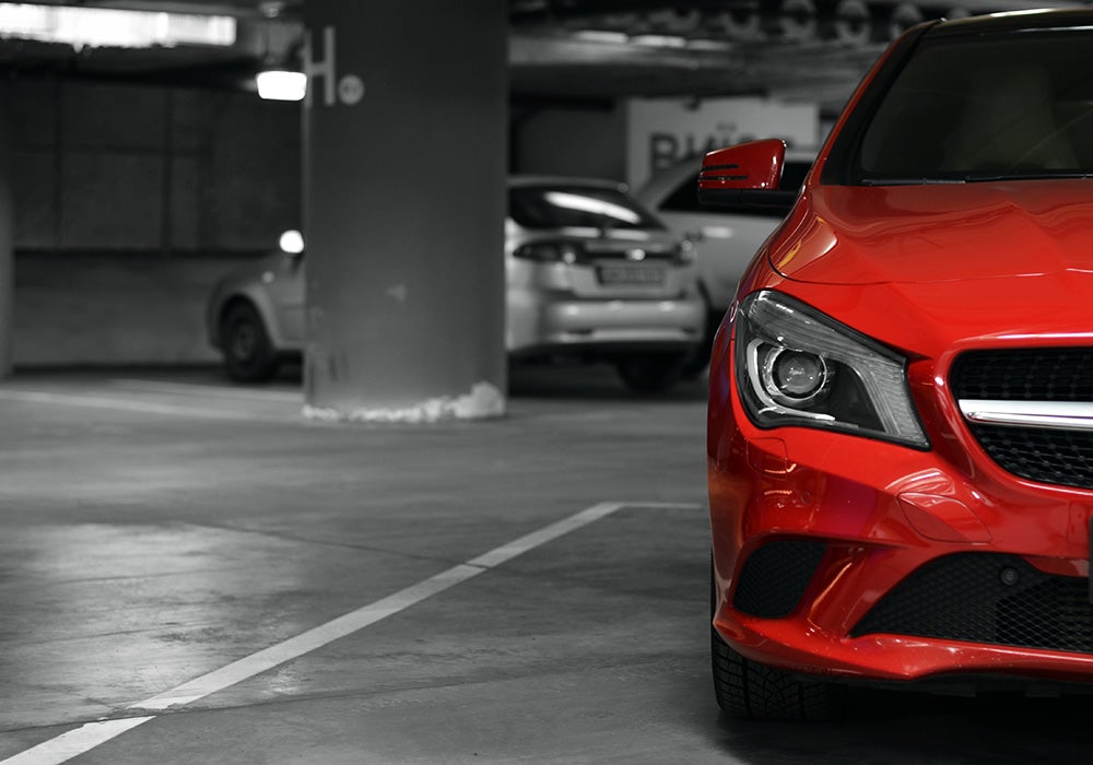 Bright red car parked in a dimly lit indoor garage with other cars in the background.
