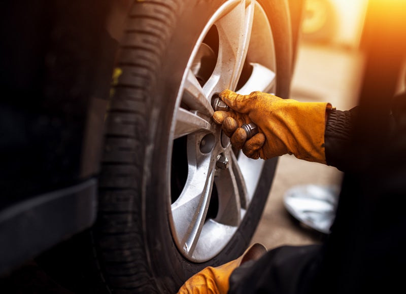 A close-up of hands wearing orange gloves working on a car tire with a wrench.